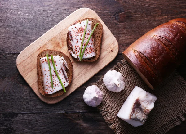 Sandwiches con manteca de cerdo sobre tabla de cortar y ajo sobre fondo de madera — Foto de Stock