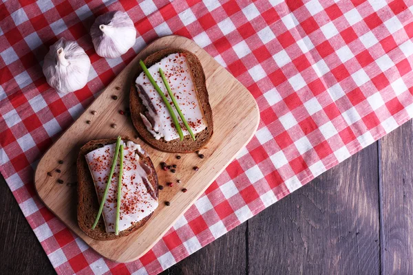 Sandwiches with lard on cutting board and garlic on table close up — Stock Photo, Image