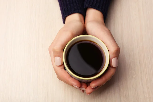 Kvinnliga händer som håller kopp kaffe på trä bakgrund — Stockfoto