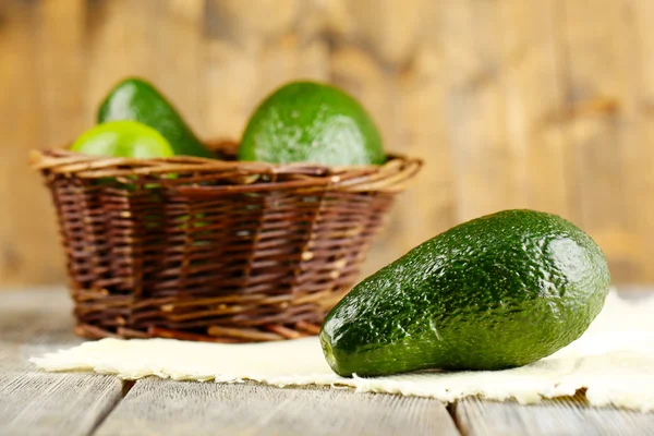 Avocado with limes in basket on wooden background — Stock Photo, Image