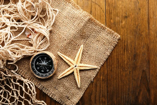 Sea stars with compass on sackcloth on wooden background — Stock Photo, Image
