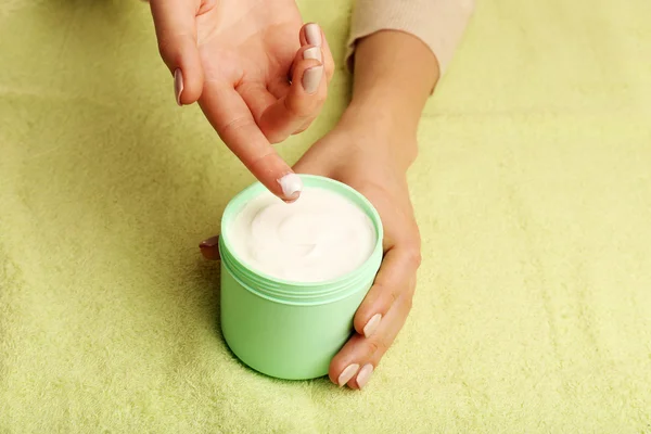 Mãos femininas com frasco de creme no fundo do tecido — Fotografia de Stock