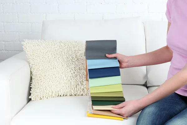 Woman sitting on sofa and chooses scraps of colored tissue — Stock Photo, Image