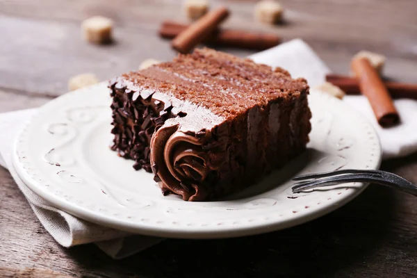 Sabroso pedazo de chocolate con terrón de azúcar y palitos de canela pastel sobre fondo de mesa de madera — Foto de Stock