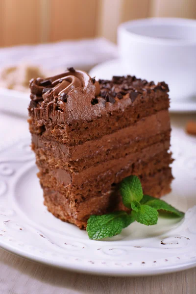 Tasty piece of chocolate cake with mint and cinnamon on wooden table and blurred planks background — Stock Photo, Image
