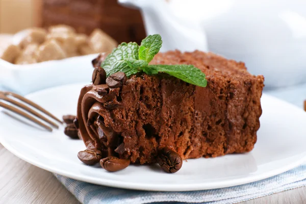 Pedaço saboroso de bolo de chocolate com hortelã e grãos de café na mesa de madeira e pranchas borradas fundo, vista close-up — Fotografia de Stock