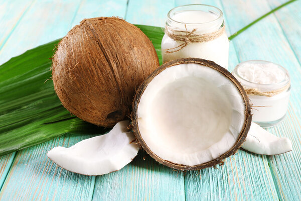 Fresh coconut oil in glassware and green leaf on color wooden table background