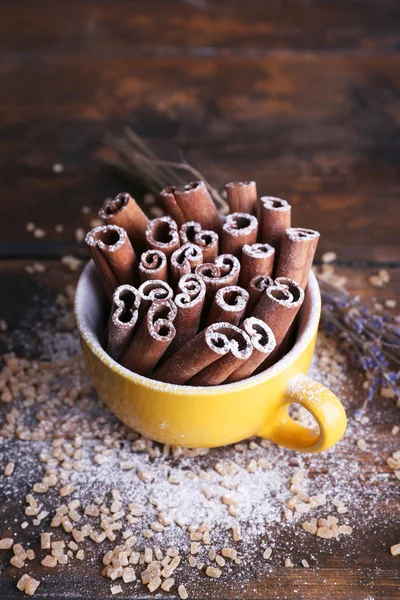 Cinnamon sticks in cup with sugar and lavender on wooden table background — Stock Photo, Image