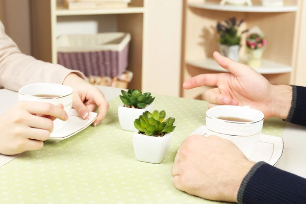 Mani femminili e maschili con tazze di tè, primo piano, sullo sfondo interno di casa — Foto Stock