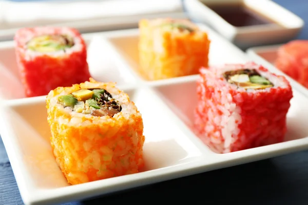 Rouleaux de sushi sur assiette, sauce soja et baguettes sur fond de bois de couleur — Photo