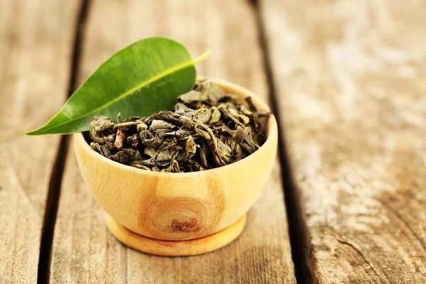 Groene thee met blad in kom op oude houten tafel — Stockfoto