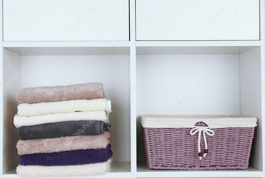 Colorful towels with wicker basket on shelf of rack background