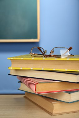 Ahşap masa, renkli duvar ve karatahta zemin üzerinde gözlüklü kitap yığını