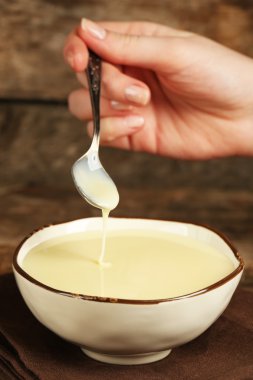 Bowl with condensed milk and spoon on table close up clipart