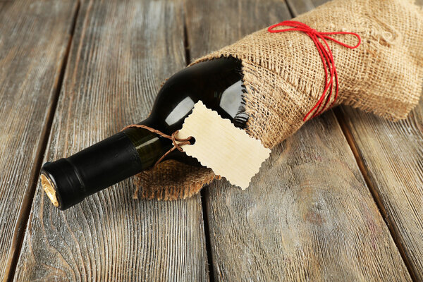 Wine bottle wrapped in burlap cloth on wooden planks background