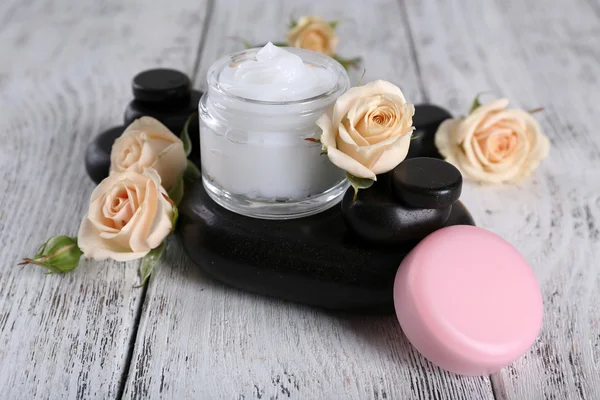 Kosmetikcreme mit Blumen und Wellness-Steinen auf Holzgrund — Stockfoto