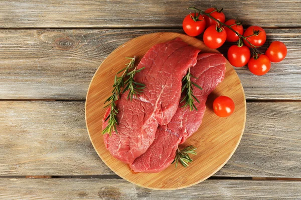 生の牛肉ステーキ ローズマリーと木製の背景にまな板の上のチェリー トマト — ストック写真