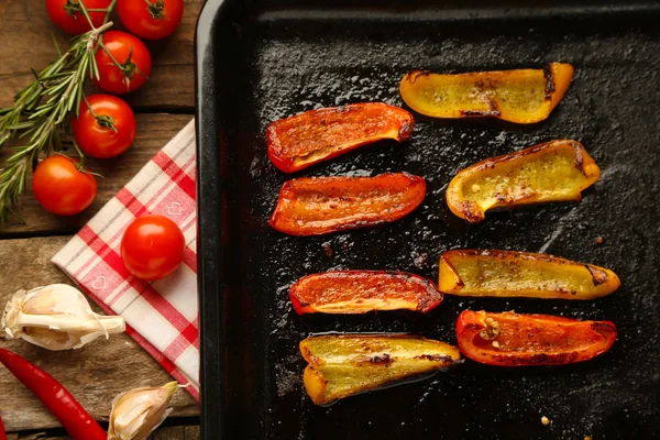 Samenstelling met geroosterde gesneden peper op pan, tomaten en rozemarijn takjes op houten achtergrond — Stockfoto