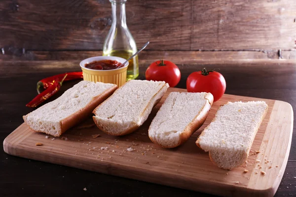 Slices of bread with tomato sauce on cutting board on wooden background — Stock Photo, Image