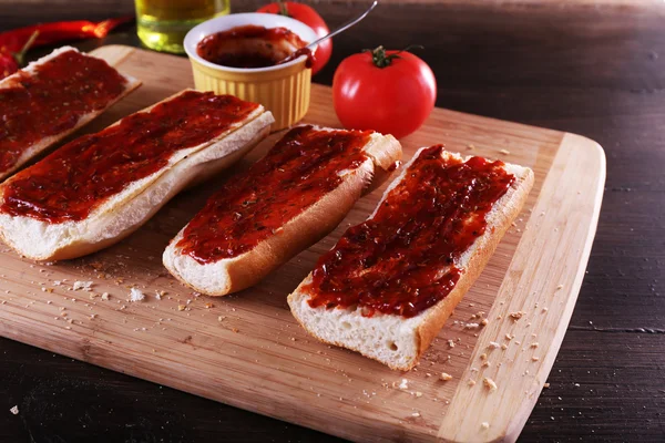 Fatias de pão com molho de tomate na tábua de corte no fundo de madeira — Fotografia de Stock