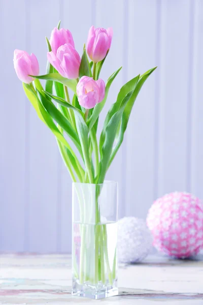 Schöne rosa Tulpen in Vase mit dekorativen Kugeln auf dem Tisch auf hölzernem Hintergrund — Stockfoto