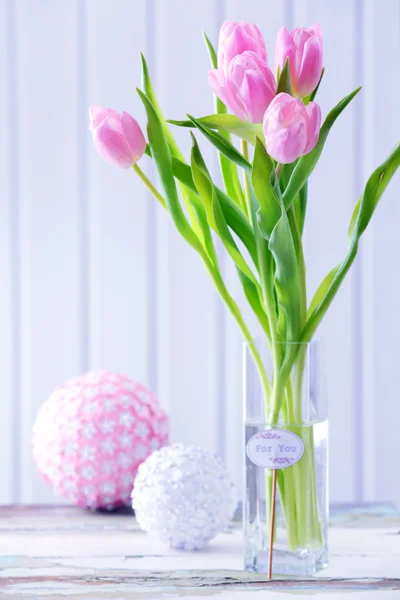 Hermosos tulipanes rosados en jarrón con bolas decorativas en la mesa sobre fondo de madera — Foto de Stock