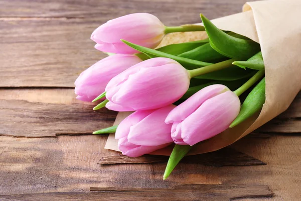 Mooie roze tulpen in papier op houten achtergrond — Stockfoto