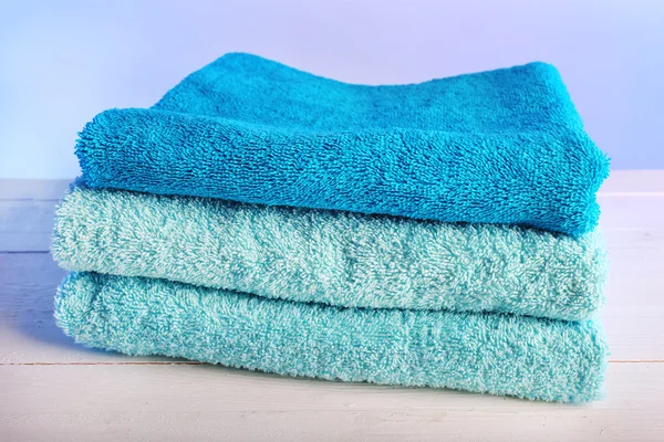 Folded towels on wooden table and light colorful background — Stock Photo, Image