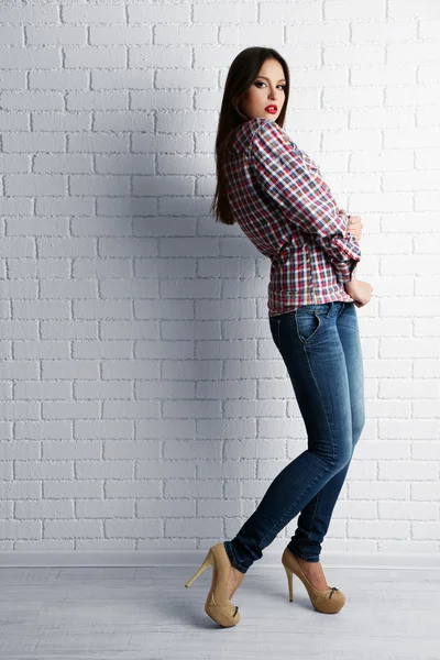 Menina bonita vestida em estilo casual posando no fundo da parede de tijolo branco — Fotografia de Stock