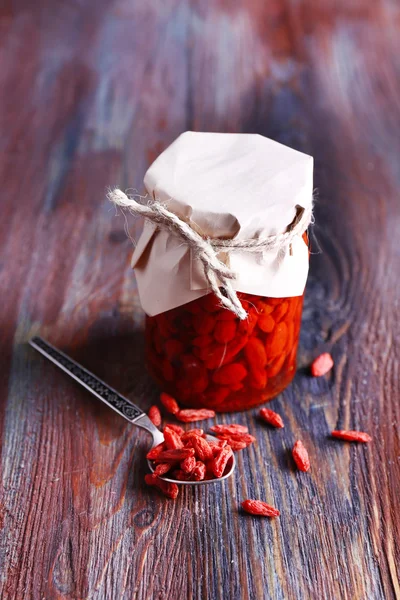Goji berries in glass bottle wrapped with paper and silver spoon on rustic wooden table background — Stock Photo, Image