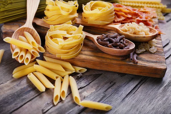 Diversi tipi di pasta su tagliere e sfondo tavolo in legno — Foto Stock