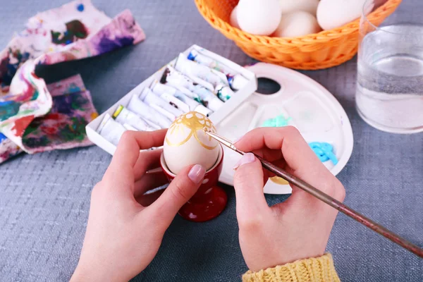 Painting Easter eggs by female hands on colorful tablecloth background — Stock Photo, Image
