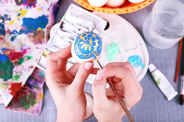 Pintura de ovos de Páscoa por mãos femininas em fundo de toalha de mesa colorido — Fotografia de Stock