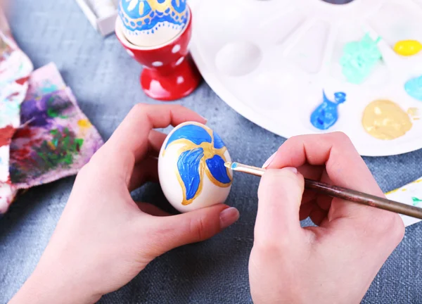 Painting Easter eggs by female hands on colorful tablecloth background — Stock Photo, Image