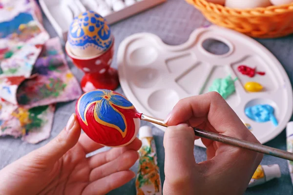 Painting Easter eggs by female hands on colorful tablecloth background — Stock Photo, Image