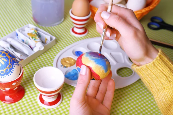 Painting Easter eggs by female hands on colorful tablecloth background — Stock Photo, Image