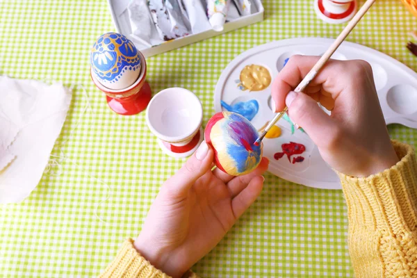 Painting Easter eggs by female hands on colorful tablecloth background — Stock Photo, Image