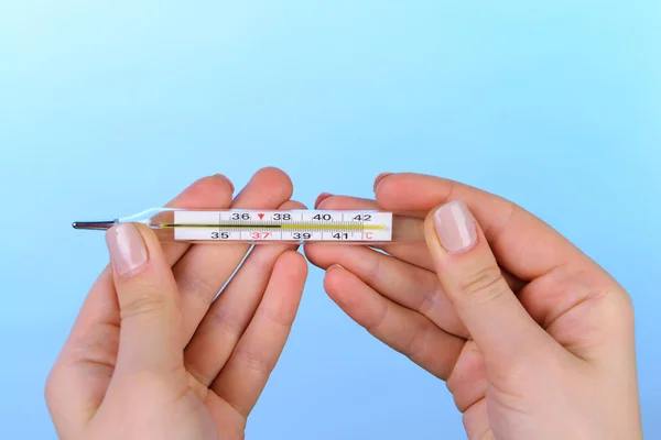 Female hands holding thermometer on blue background — Stock Photo, Image