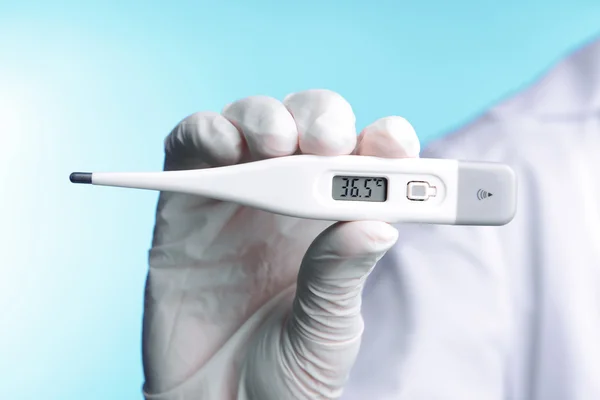 Doctor sosteniendo termómetro sobre fondo azul —  Fotos de Stock