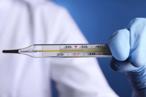 Arzt hält Thermometer auf blauem Hintergrund — Stockfoto