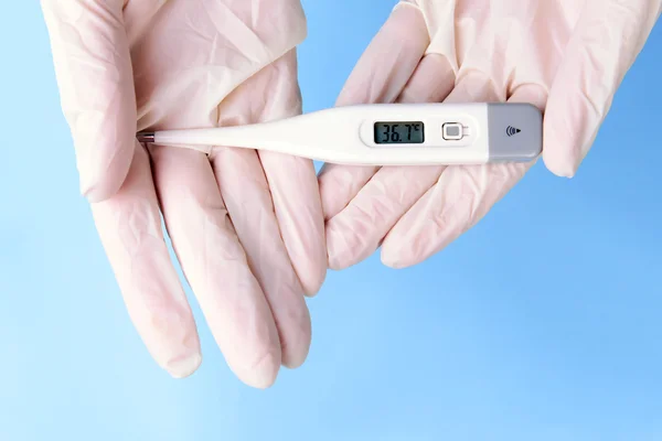 Hands with gloves holding thermometer on blue background — Stock Photo, Image