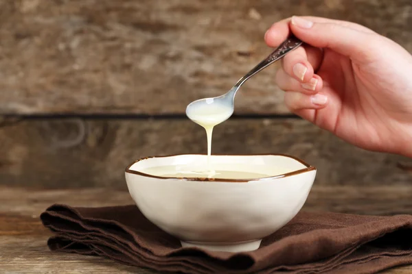 Cuenco con leche condensada y cuchara en servilleta sobre fondo de madera — Foto de Stock