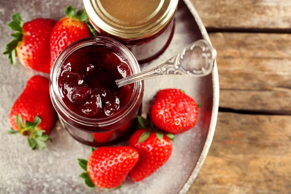 Jars of strawberry jam with berries on tray on table close up — Stock Photo, Image