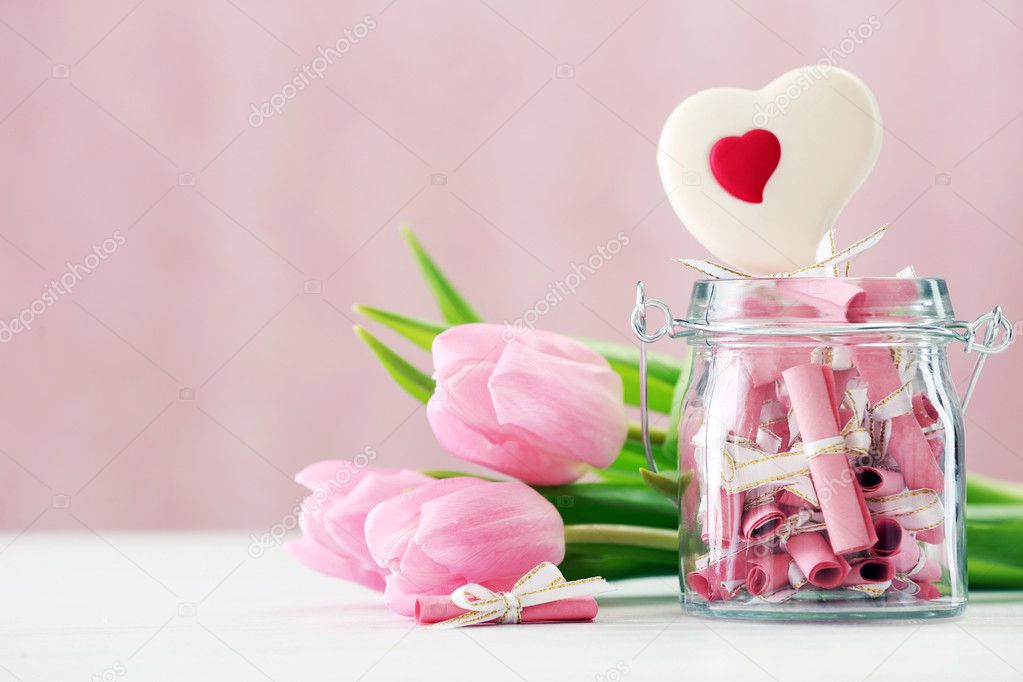 Beautiful pink tulips with jar of papers  on table on bright background