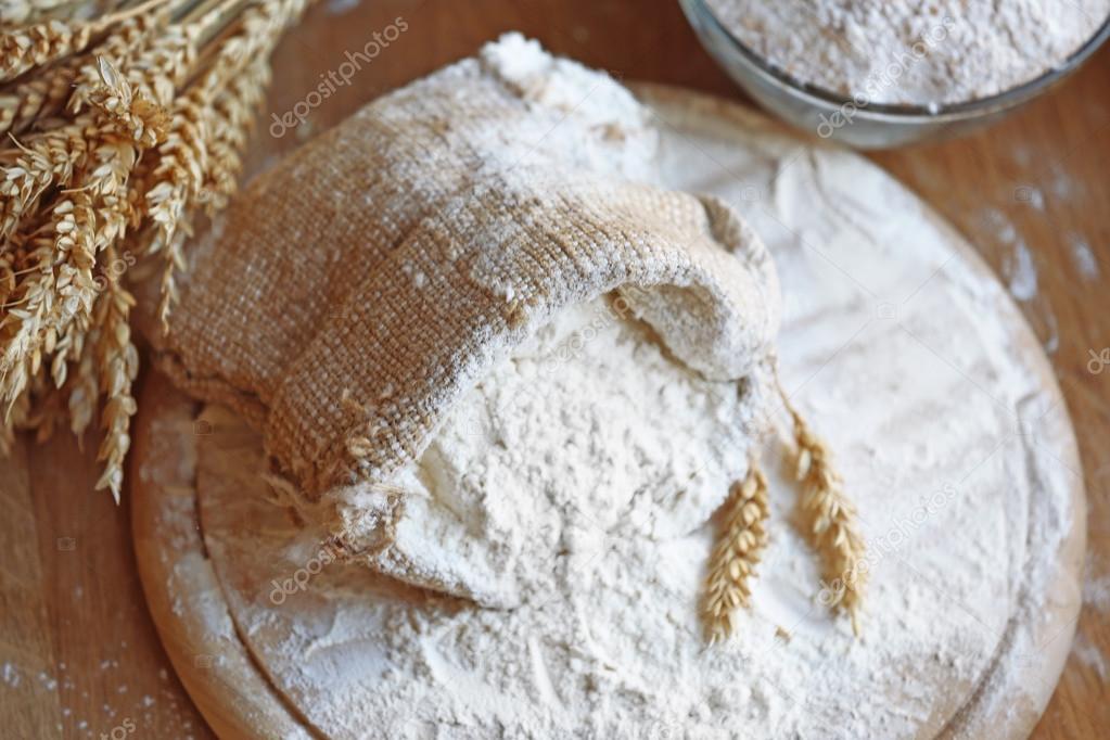 Flour in burlap bag on cutting board and wooden table background