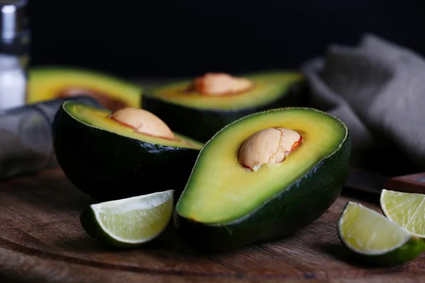 Sliced avocado with lime on wooden cutting board on black background — Stock Photo, Image