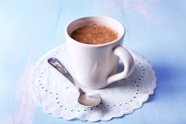 Cup of cocoa with spoon on napkin on wooden background — Stock Photo, Image