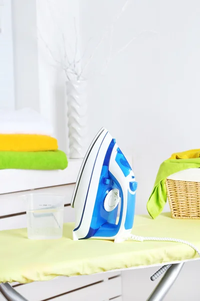 Iron and clothes on ironing board on interior background — Stock Photo, Image