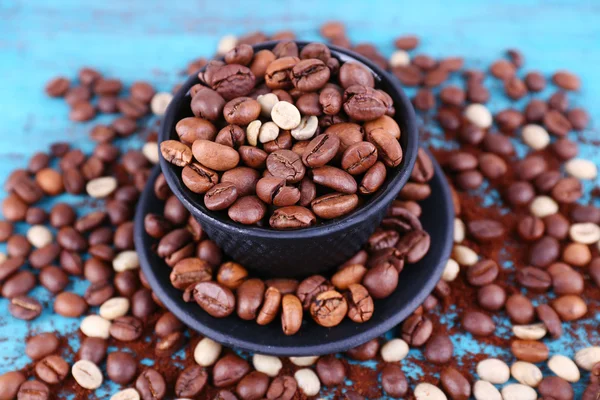 Kaffeebohnen in schwarzer Keramiktasse auf blauem Holzhintergrund — Stockfoto