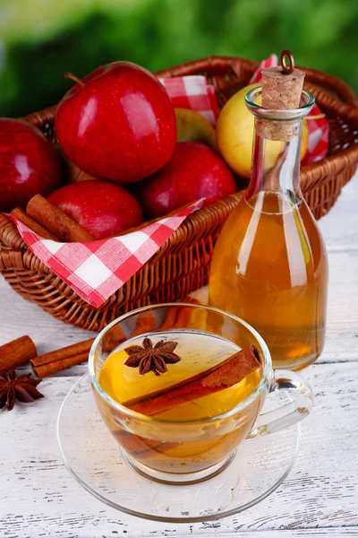 Apple cider with cinnamon sticks and fresh apples in wicker basket on wooden table, on bright background — Stock Photo, Image